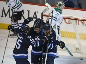 Jets forwards Mark Scheifele, left, and Andrew Copp, right, congratulate Patrik Laine on his game-winning goal against the Dallas Stars during their game in Winnipeg on Tuesday night.