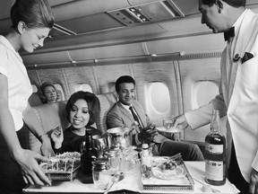 Flight crew serving food and beverages to passengers aboard an airplane, 1960s.