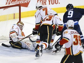 Flames goalie Brian Elliott saves the shot by the Jets' Andrew Copp as Calgary's TJ Brodie and Sean Monahan defend during third period action in Winnipeg on Saturday night.