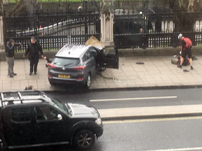 People stand near a crashed car and an injured person lying on the ground, right, on Bridge Street near the Houses of Parliament in London, Wednesday, March 22, 2017.