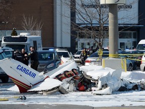 A firefighter and police officers look at the wreckage from a plane crash sits in a parking lot in Saint-Bruno, Que., on Friday, March 17, 2017. Two small planes have collided over a major shopping mall