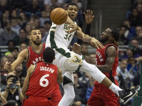 Giannis Antetokounmpo of the Bucks passes the ball after being stopped by Toronto Raptors' Jonas Valanciunas, left, DeMarre Carroll, right, and Cory Joseph during the first half of their game Saturday night in Milwaukee.