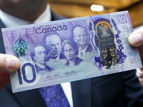 Stephen Poloz, governor of the Bank of Canada, stands for a photograph with a copy of a commemorative $10 note at Bank of Canada headquarters in Ottawa, Ontario, Canada, On Friday, April 7, 2017.