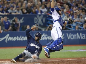 Keon Broxton of the Milwaukee Brewers slides across home plate to score a run in the third inning as Blue Jays catcher Russell Martin  leaps for an errant throw at Rogers Centre in Toronto on Tuesday night.