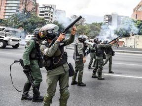 Venezuelan National Guard personnel in riot gear fire tear gas grenades during a march of opposition activists