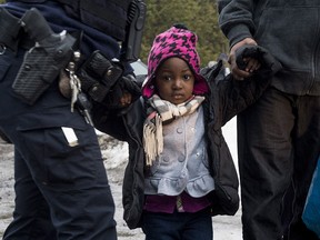 An young asylum claimant is held by an RCMP officer and her father after crossing the border into Canada from the United States, Tuesday, March 28, 2017 near Hemmingford, Que.