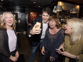 Prime Minister Justin Trudeau records a video greeting for the brother of Andrea Hughes', second from right, who went to school with Trudeau, as Liberal candidate for Ottawa-Vanier Mona Fortier, left, and Roxane Pothakos, right, look on, as they meet with constituents in the riding ahead of a by-election, in Ottawa on Friday, March 24, 2017.
