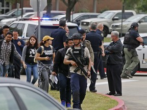 An officer leads a group of students walking out of the building as Irving police officers work at a fatal shooting scene on the North Lake College