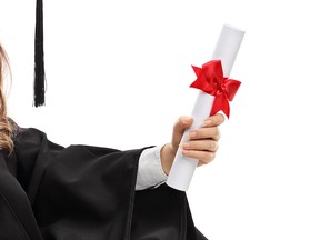 Happy graduate student with a diploma sitting on the floor and leaning against a wall isolated on white background
