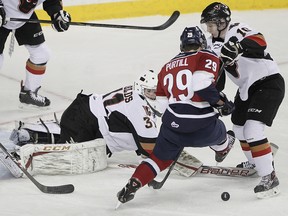 Chase Lang of the Calgary Hitmen and Braden Purtill  of the Tri-City Americans jostle in front of Calgary Hitmen goalie Mack Shields during WHL action in Calgary, Alta.
