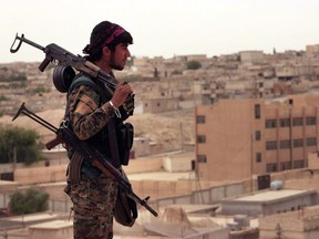 This April 30, 2017 photo provided by the Syria Democratic Forces (SDF), shows a fighter from the SDF carrying weapons as he looks toward the northern town of Tabqa, Syria.