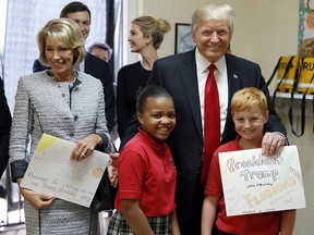 In this March 3, 2017 photo, President Donald Trump and Education Secretary Betsy DeVos pose with fourth graders Janayah Chatelier, 10, left, Landon Fritz, 10, after they received cards from the children, during a tour of Saint Andrew Catholic School in Orlando, Fla.