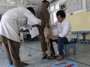 In this Saturday, June 17, 2017, photo, physiotherapists, left, and right, adjust an artificial leg of a land mine victim at the International Committee of the Red Cross (ICRC) physical rehabilitation center in Kabul, Afghanistan. Afghans who scratch out a living by removing some of the country's countless land mines have long had to contend with rugged terrain, accidental explosions and the threat of kidnapping _ but these days they face the added risk of being laid off.  (AP Photo/Rahmat Gul)