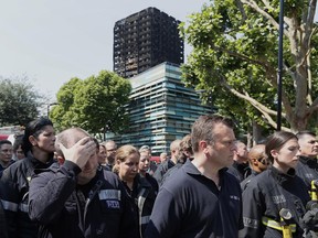 Emergency services workers take part in a minute's silence in front of Grenfell Tower in London, Monday, June 19, 2017. Tens of people died when a fire engulfed the high-rise apartment block in west London last week.(AP Photo/Kirsty Wigglesworth)