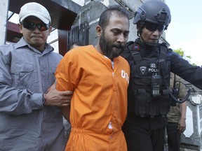Indonesian police officers escort Indian inmate Sayed Mohammed Said, center, upon his return at Bali international airport, Indonesia, Saturday, June 24, 2017. Authorities in East Timor arrested two foreign inmates, including Said, who escaped from a prison in neighboring Indonesia's resort island of Bali, police said. The two were among four foreign inmates who escaped Monday from the Kerobokan penitentiary in Bali through a 50-by-70-centimeter (20-by-28-inch) hole found under the walls that connects to a 15-meter-long (49-foot-long) water tunnel heading toward a main street. (AP Photo/Firdia Lisnawati)