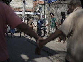 In this June 12, 2017 photo, men pray before eating a free meal provided by resident Ana Regina de Jesus in the City of God slum of Rio de Janeiro, Brazil. Only about 60 of the usual 150 showed up because of a nearby shooting. (AP Photo/Leo Correa)