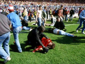 FILE - In this April 15, 1989 file photo, police, stewards and supporters tend and care for wounded supporters on the pitch at Hillsborough Stadium, in Sheffield, England. British prosecutors on Wednesday June 28, 2017, are set to announce whether they plan to lay charges in the deaths of 96 people in the Hillsborough stadium crush _ one of Britain's worst-ever sporting disasters. (AP Photo, File)