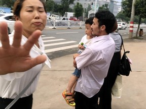 Hua Xiaoqin, left, sister of Chinese labor activist Hua Haifeng, tries to block a reporter approaching Hua Haifeng, right, as he carries his son Bobo leaves a police station after being released in Ganzhou in southern China's Jiangxi Province, Wednesday, June 28, 2017. Chinese authorities have released on bail three activists who had been detained after investigating labor conditions at a factory that produced shoes for Ivanka Trump and other brands. (AP Photo/Gerry Shih)