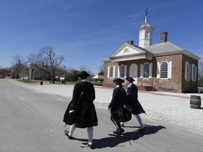 In a Wednesday March 18, 2015 file photo, Colonial interpreters walk in front of the Colonial courthouse along Duke of Gloucester street in the Colonial Williamsburg area of Williamsburg, Va. Colonial Williamsburg, facing a decline in visitors and hundreds of millions in debt, announced Thursday it will outsource many of its commercial operations in a restructuring that will include layoffs. (AP Photo/Steve Helber, File)