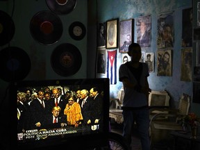 FILE - In this June 16, 2017, file photo, a man walks past a television set showing U.S. President Donald Trump signing the new Cuba policy, in a living room festooned with images of Cuban leaders at a house in Havana, Cuba. President Trump declared he was restoring some travel and economic restrictions on Cuba that were lifted as part of the Obama administration's historic easing. (AP Photo/Ramon Espinosa, File)