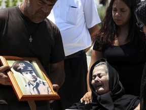 In this Saturday, June 10, 2017 photo, Eleni Kyriakou, 88, right, mother of 20-year-old Epiphanios Kyriakou who went missing in  1974 during the  Turkish invasion, seen in portrait, left, mourns  during his funeral at a military cemetery at Makedonitissa in divided capital Nicosia, Cyprus. Over 11 years of work, Cyprus' Committee on Missing Persons has worked diligently to help heal a gaping wound from this tiny east Mediterranean island's tumultuous past. (AP Photo/Petros Karadjias)