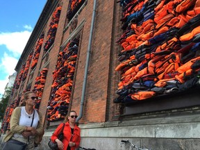 People walk past the new artwork entitled 'Soleil Levant' (sunrise in French) by Chinese dissident artist Ai Weiwei, made from over 3,500 lifejackets discarded by migrants on the Greek island of Lesbos, following its official inauguration at Copenhagen's Kunsthal Charlottenborg museum in Copenhagen, Denmark, Tuesday June 20, 2017.  Weiwei has barricaded the windows of the museum for his provocative new artwork as a striking reminder of the ongoing migrant crisis, inaugurated Tuesday on World Refugee Day.  (AP Photo / James Brooks)