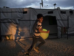 In this Monday, May 29, 2017 photo a Syrian boy runs as he carries a giant tennis ball at the refugee camp of Ritsona about 86 kilometers (53 miles) north of Athens. On World Refugee Day, more than 60,000 refugees and migrants are still stranded in Greece in a process barely moving: Forward to other countries of the European Union, or back to Turkey under a deportation deal launched 15 months ago. (AP Photo/Petros Giannakouris)