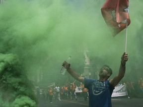 A protester reacts next to a flare outside the the Interior Ministry as thousands of striking municipal workers demonstrate in central Athens, Thursday, June 22, 2017. Union officials want the left-led government to grant full-time, permanent state jobs to municipal workers employed on short-term contracts that have expired or are about to expire. (AP Photo/Petros Giannakouris)