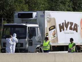 FILE - In this Aug. 27, 2015 file photo, investigators stand near an abandoned truck on the shoulder of Highway A4 near Parndorf, Austria, south of Vienna. Officials said they discovered 71 badly decomposed bodies of men, women and children, inside and that some may never be identified.  The  trial of 11 alleged human smugglers indicted for the deaths of 71 migrants who suffocated in the back of a refrigerated truck in 2015 starts in Kecskemet, Hungary, Wednesday June 21, 2017.  (AP Photo/Ronald Zak,file)