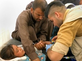 A man comforts his daughter as a doctor treats her after she was taken ill with suspected food poisoning in the Hassan Sham U2 camp for displaced people located about 20 kilometres east of Mosul