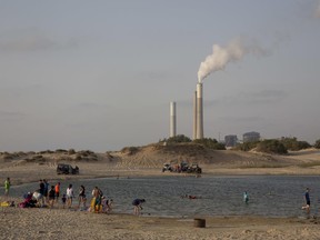 Israel's electricity power plant in Ashkelon is seen as people bath near kibbutz Zikim, on the Israel Gaza Border, Monday, June 19, 2017. Israel's national electric company on Monday cut back its already limited electricity shipments to the Gaza Strip in a step that is expected to worsen the power crunch plaguing the Hamas-controlled seaside territory. The company confirmed that the Israeli government instructed it to reduce the power supply to Gaza at the request of the Palestinian President Mahmoud Abbas' government in the West Bank. (AP Photo/Ariel Schalit)