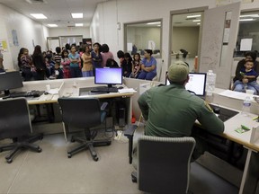 FILE - This June 18, 2014, file photo shows U.S. Customs and Border Protection agents work at a processing facility in Brownsville,Texas. A new "surge initiative" aims to identify and arrest the adult sponsors of unaccompanied minors who paid coyotes or other smuggling operations to bring young people across the U.S. border, Immigration and Customs Enforcement officials confirmed Thursday, June 29, 2017. (AP Photo/Eric Gay, Pool, File)