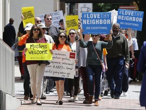 FILE- In this May 8, 2017, file photo, protesters hold signs and march outside the US 4th Circuit Court of Appeals in Richmond, Va. A federal judge said Wednesday, June 21, that a class-action lawsuit challenging a once-secret government program that delayed immigration and citizenship applications by Muslims can move forward. (AP Photo/Steve Helber, file)