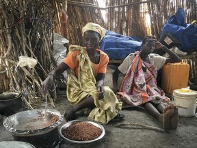 In this photo taken Monday, June 19, 2017, Elizabeth Adwok, left, an ethnic Shilluk who arrived with her seven children in April after having been forcefully displaced from her home three times since South Sudan's conflict began, cooks sorghum in her small hut in the village of Aburoc, South Sudan where she lives with other displaced people. A new report by Amnesty International says South Sudanese forces burned, shelled and ransacked homes between January and May, killing civilians and forcing thousands from the Shilluk ethnic minority to flee. (AP Photo/Sam Mednick)