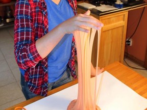 In this June 21, 2017 photo, Astrid Rubens demonstrates the elasticity of homemade slime in her kitchen in St. Paul, Minn.  Glue, baking soda and contact lens solution are all it takes to make satisfyingly stretchy slime. (AP Photos/Jeff Baenen)