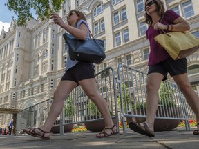 Pedestrians walk by the security fence in front of the Trump International Hotel in Washington, Wednesday, June 28, 2017. President Donald Trump will attend a fund raiser at the hotel this evening. (AP Photo/J. David Ake)