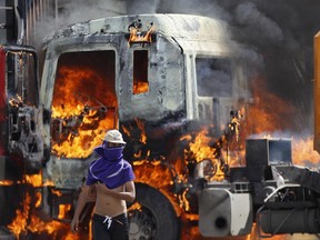 A masked demonstrator walks near a flaming truck, seized and set on fire by demonstrators, during an anti-government protest on the Francisco Fajardo highway, outside La Carlota Air Base in Caracas, Venezuela, Friday, June 23, 2017. More than 70 people have been killed during almost 90 days of protests seeking President Nicolas Maduro's removal. (AP Photo/Ariana Cubillos)