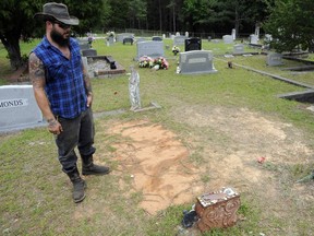 In this Wednesday, May 3, 2017 photo, Tyler Goodson of the hit podcast "S-Town" stands at the grave in Green Pond, Ala., of friend John B. McLemore, who is also featured in the serialized show. A judge has set an Oct. 16 trial date for Goodson, named in a mulit-count indictment related to an alleged theft linked to events in the popular story.  Goodson has pleaded not guilty to a multi-count indictment alleging he took lumber, old vehicles and a laptop computer from the property of his friend John B. McLemore, the main character in "S-Town." (AP Photo/Jay Reeves)