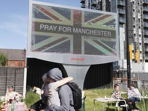 FILE - This is a Tuesday May 23, 2017 file photo of a couple as they embrace under a billboard in Manchester  in England Tuesday May 23, 2017, the day after the suicide attack at an Ariana Grande concert that left more than 20 people dead . British police said Thursday July 6, 2017, that the man who bombed an Ariana Grande concert in Manchester wasn't part of a large network, but other people involved in the attack may still be at large.  (AP Photo/Kirsty Wigglesworth/File)