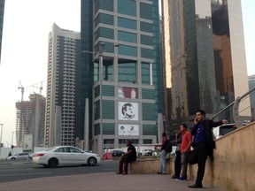 FILE - In this Sunday, July 9, 2017 file photo, men wait for a bus in front of a building with the poster of Qatari Emir Sheikh Tamim bin Hamad Al Thani. It's been more than a month since four Arab nations cut land, sea and air routes to Qatar, but in the gas-rich Gulf nation's glimmering malls and luxury hotels there is little sign of hardship. (AP Photo/Maggie Hyde, File)