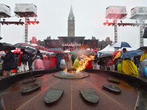 People take shelter from the rain on Parliament Hill as the Centennial Flame burns in Ottawa during Canada 150 celebrations