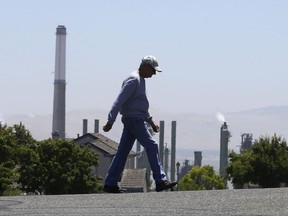 The stacks from the Valero Benicia Refinery are seen as a pedestrian walks in a nearby neighborhood, Wednesday, July 12, 2017, in Benicia, Calif. California Gov. Jerry Brown is racing to convince state lawmakers to extend California's cap-and-trade program which puts a price on carbon emitted by polluters, including oil refineries. The program has been closely watched around the world as a market-based way to reduce greenhouse gas emissions, but it expires in 2020. (AP Photo/Rich Pedroncelli)