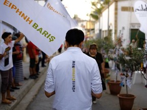 A peace protestor with a t-shirt "United Cyprus Now" takes part in a peace demonstration as people wave flags reading in Greek "Peace", in Ledra crossing point inside the U.N buffer zone in central divided capital, Nicosia, Cyprus, Wednesday, July 5, 2017. President Nicos Anastasides, a Greek Cypriot, told reporters before another session of the ongoing talks in Switzerland that he expects the Turkish and Turkish Cypriot participants to "demonstrate the same good will" to break the stalemate. (AP Photo/Petros Karadjias)