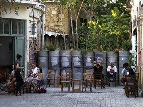 People sit outside of a cafe in front of a blocked road with barrels and sand bags by the U.N buffer zone that divides the Greek south from the Turkish Cypriot breakaway north part of the divided capital Nicosia, Cyprus, on Tuesday, July 4, 2017. At talks to end Cyprus' 43-year ethnic divide at the Swiss ski resort of Crans-Montana, Turkish Foreign Minister Mevlut Cavusoglu, made it clear that a peace accord would not include a specific, agreed-upon date by which all Turkish troops would have to be pulled out. (AP Photo/Petros Karadjias)
