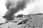 Destroyed landing craft on fire with Canadian dead on the beach following the Dieppe raid.