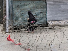 A burqa-clad Kashmiri woman walks past a barbed-wire road checkpoint set up by Indian security forces in Srinagar, Indian controlled Kashmir, Friday, July 7, 2017. Government forces imposed curfew-like restrictions in many parts of Indian controlled Kashmir to stop anti Indian protests ahead of the first death anniversary of rebel leader Burhan Wani on Saturday. His killing by security forces last year sparked violent street clashes and almost daily protests throughout the region. (AP Photo/Dar Yasin)