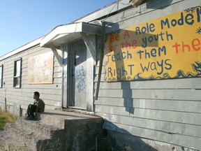 A boy sits outside the Pikangikum First Nation band office. Signs displaying positive messages line public buildings through town.