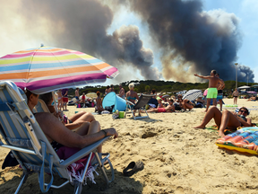 People enjoy the beach as a wildfire burns a nearby forest in Bormes-les-Mimosas, France, on July 26, 2017. At least 12,000 people, including thousands of tourists, were evacuated overnight after a new wildfire broke out.