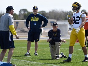 FILE - In this Feb. 29, 2016, file photo, Michigan's head coach Jim Harbaugh, center right, watches defensive coordinator Don Brown, left, work with Cheyenn Robertson during NCAA college football practice in Bradenton, Fla. The two-a-day football practices that coaches once used to toughen up their teams and cram for the start of the season are going the way of tear-away jerseys and the wishbone formation. (Tiffany Tompkins/The Bradenton Herald via AP, File)
