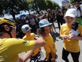 Britain's Geraint Thomas, wearing the overall leader's yellow jersey, left, signs an autograph prior to the start of the fifth stage of the Tour de France cycling race over 160.5 kilometers (99.7 miles) with start in Vittel and finish in La Planche des Belles Filles, France, Wednesday, July 5, 2017. (AP Photo/Christophe Ena)